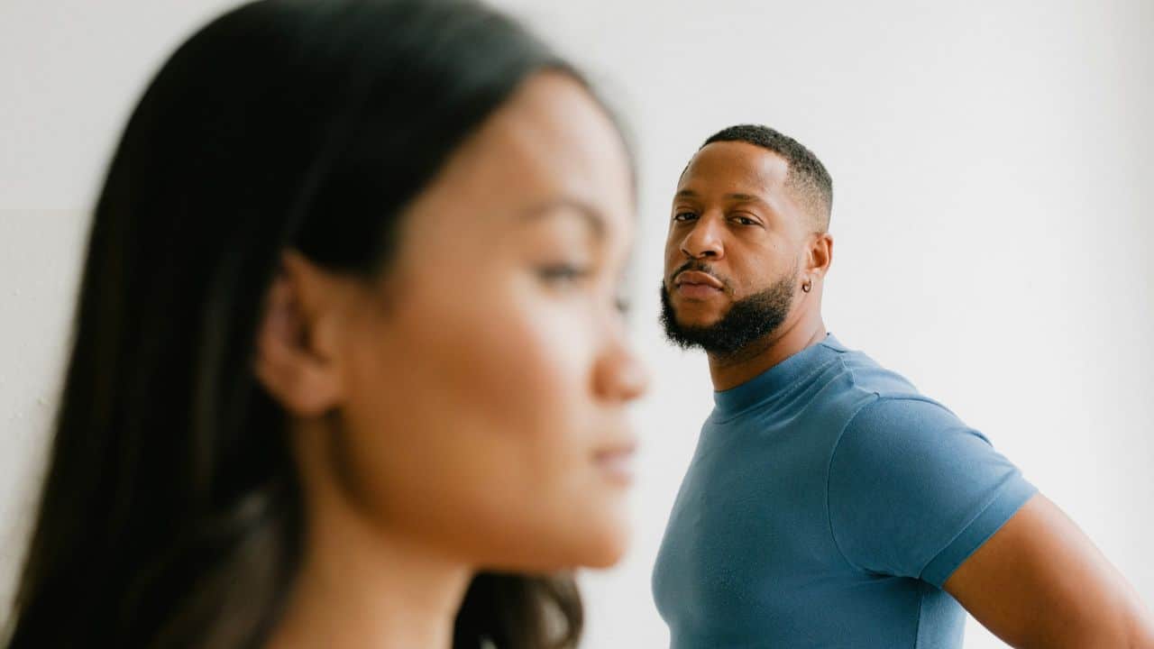 A man in a blue shirt looks toward a woman who is blurred in the foreground.
