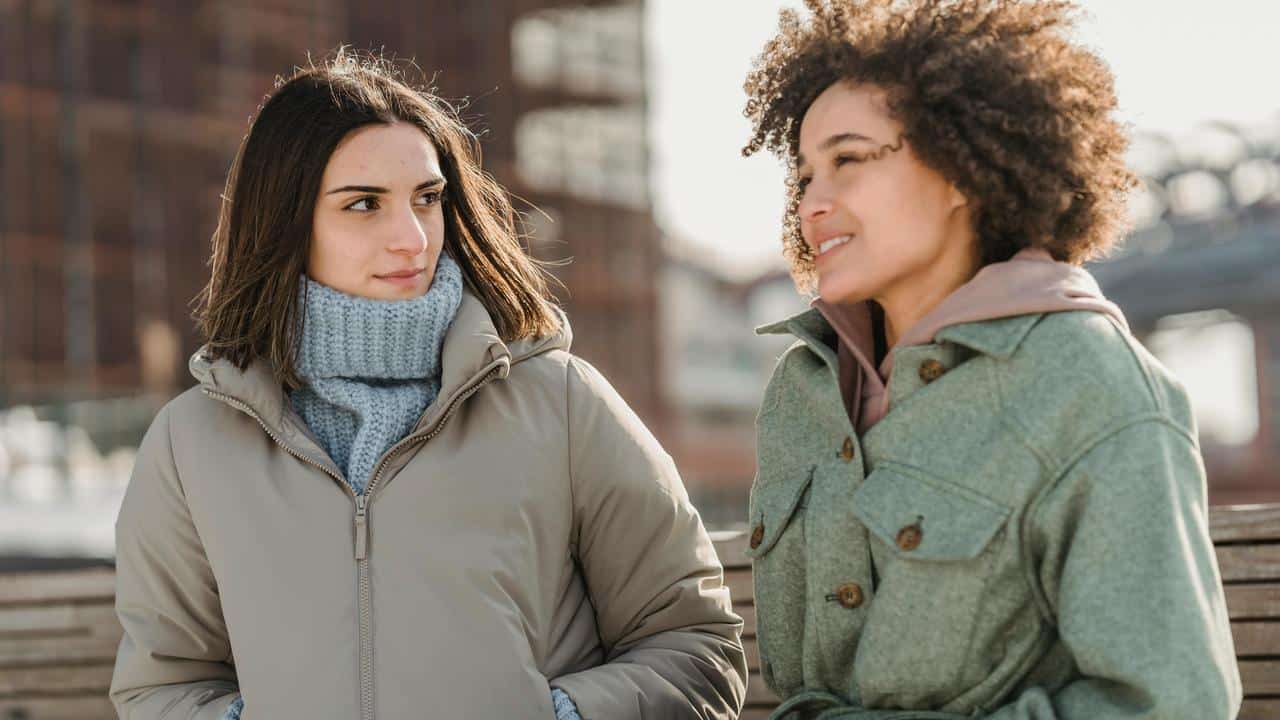 A pair of women in coats talking outdoors in a city setting.
