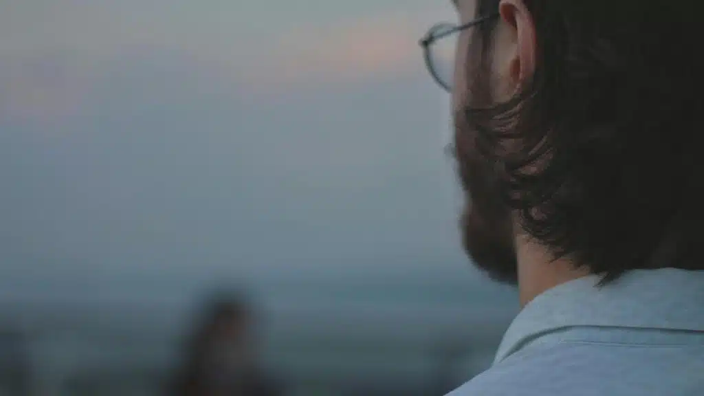 A man looking out over the ocean at dusk, seen from behind.