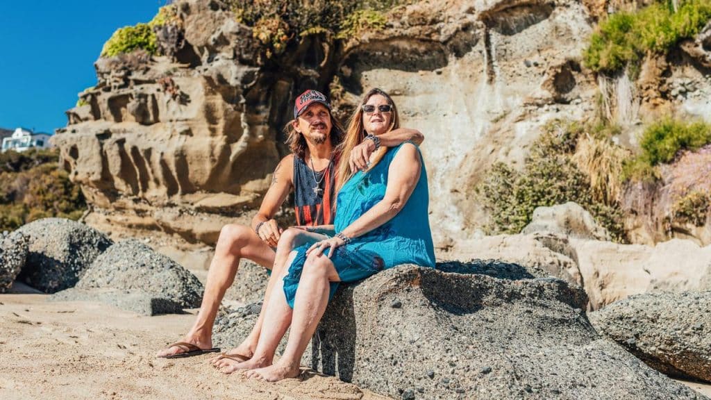 A couple sitting together on rocks at a sunny beach.