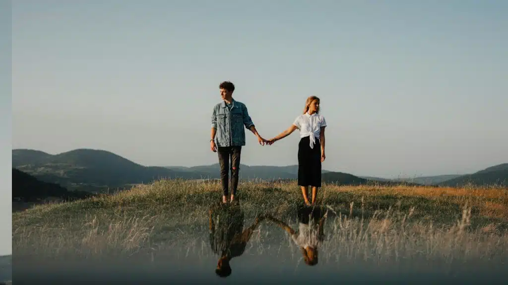 A coupke holding hands yet standing apart outdoors.