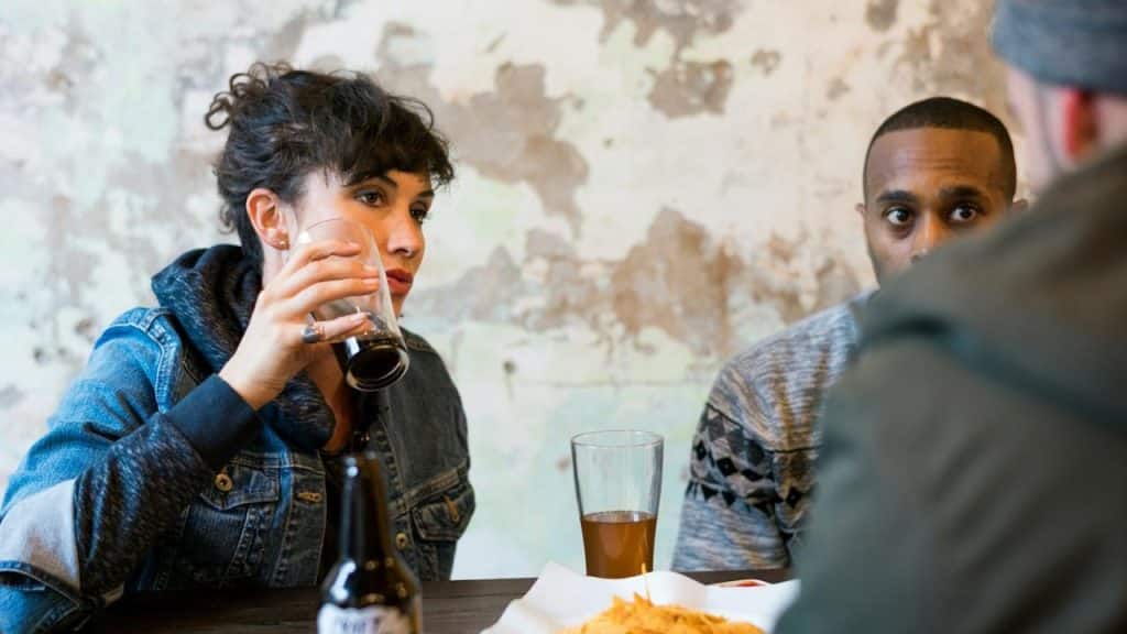 A man and a woman are drinking alcohol at a cafe, and another man is looking at them.