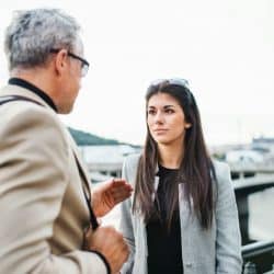 A mature man and a young woman are walking by a river in the city of Prague talking.