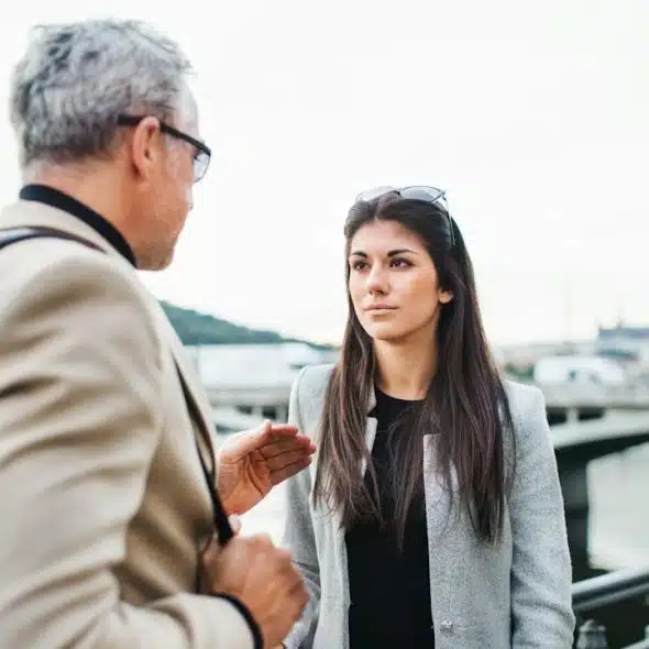 A mature man and a young woman are walking by a river in the city of Prague talking.