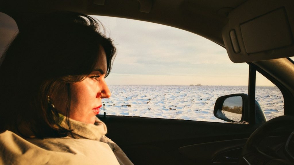 A serious-looking woman is driving a car in the snow.