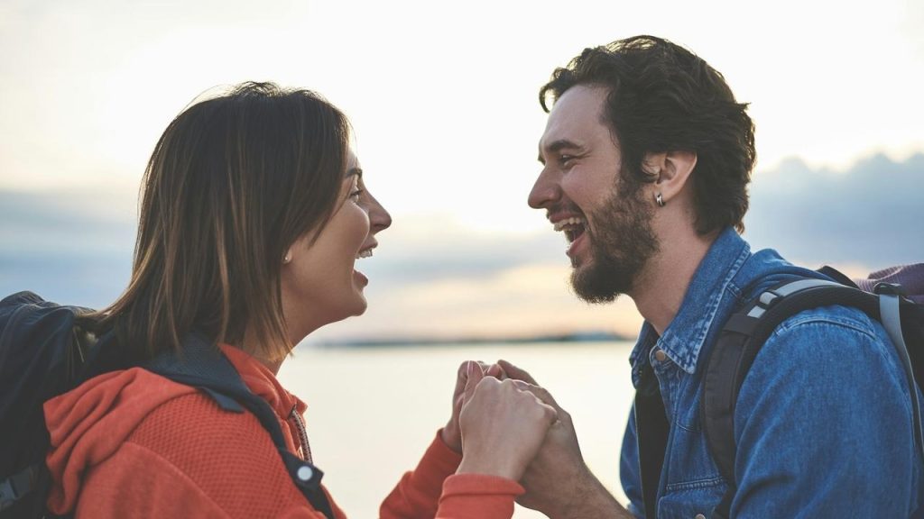 A couple laughing and holding hands outdoors.