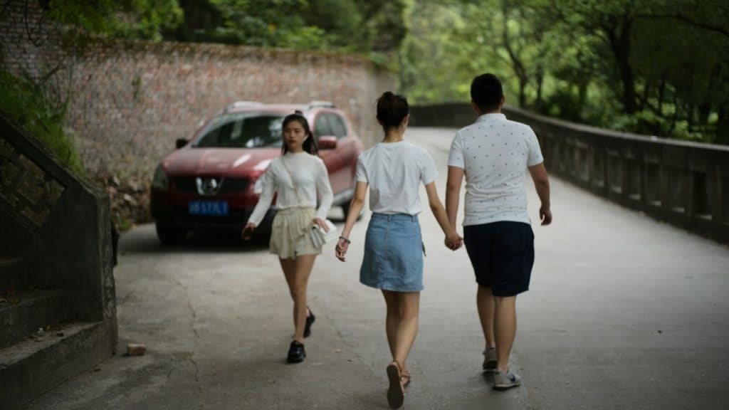 Two people are walking hand-in-hand on a path while a woman is walking opposite to them.