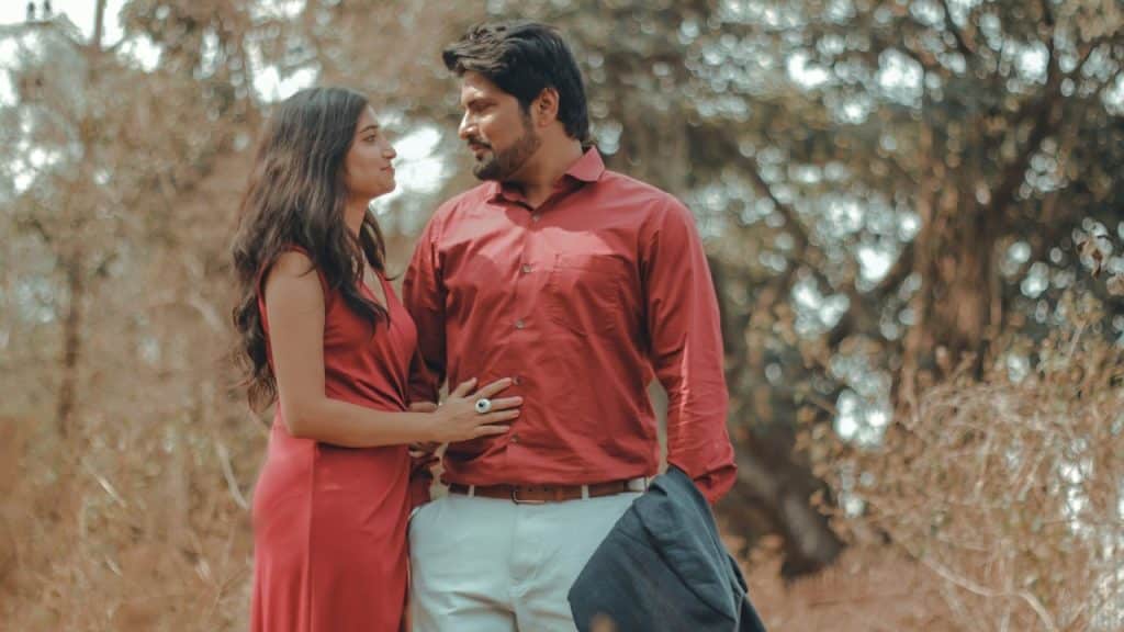 A couple, both wearing red shirts, is standing in a forest.