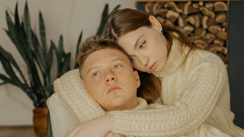 A woman is hugging her upset boyfriend indoors.