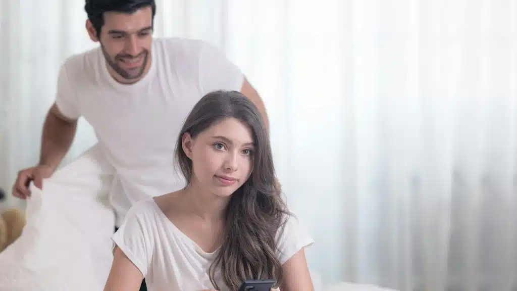 A man looking at his wife using a phone while standing behind her.
