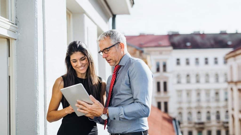 A man and woman, business partners, with a tablet, standing on a terrace in an office.