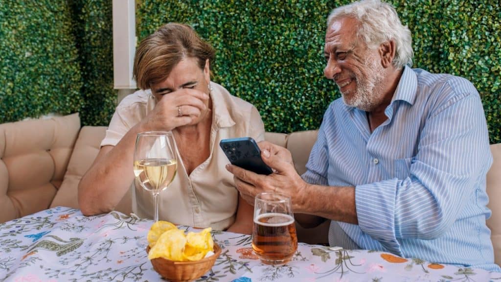An elderly couple laughs while looking at a phone together.