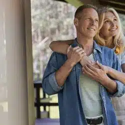A woman hugging a man from behind while they are standing on the terrace.