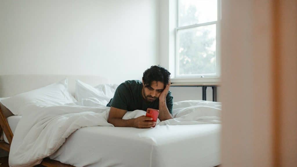 A man using a mobile phone while lying on the bed.