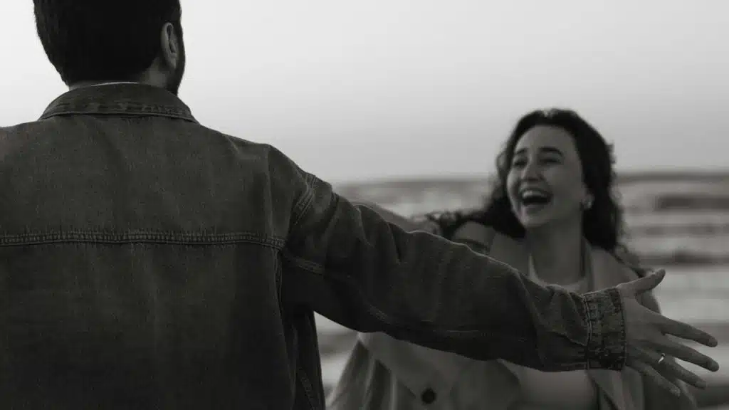 A man with open hands standing in front of a laughing woman who is coming towards him.