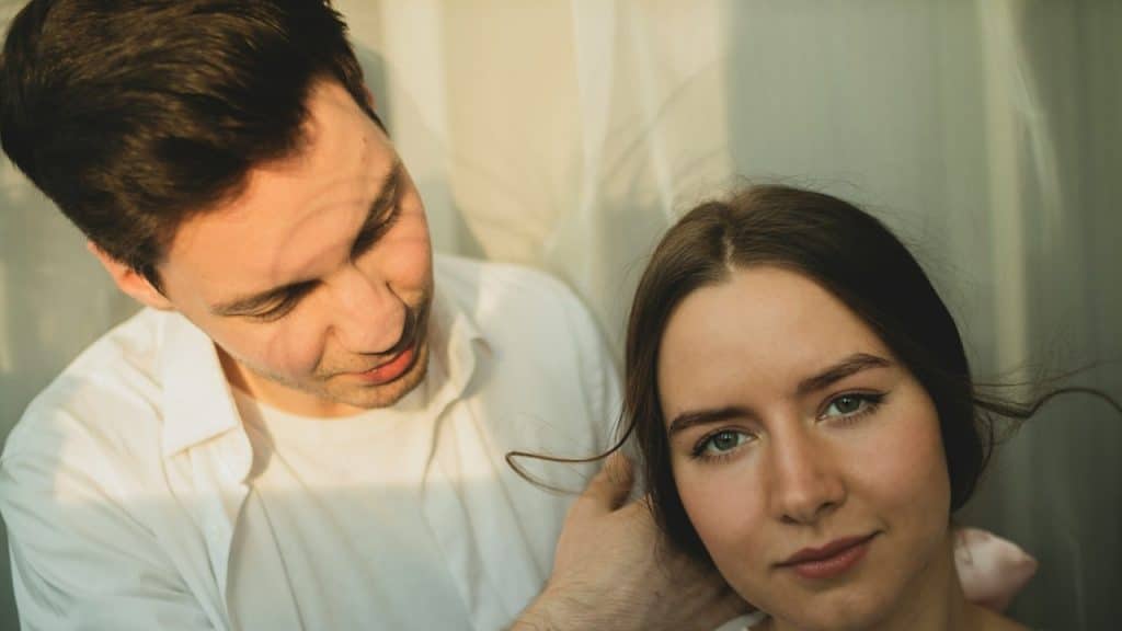 A man adjusting a woman’s hair as she looks at the camera.