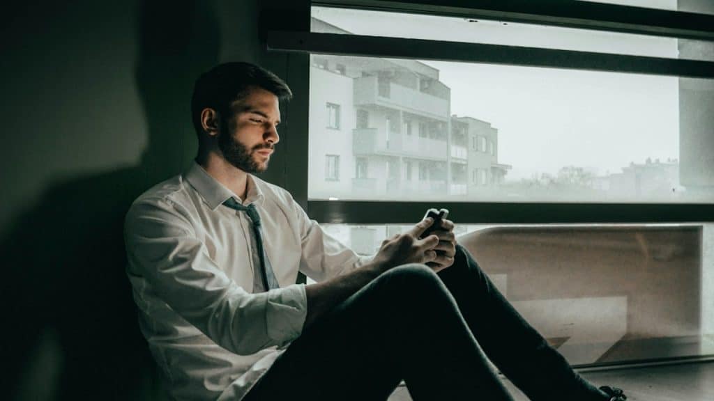 A man is using his cellphone while sitting on the floor.