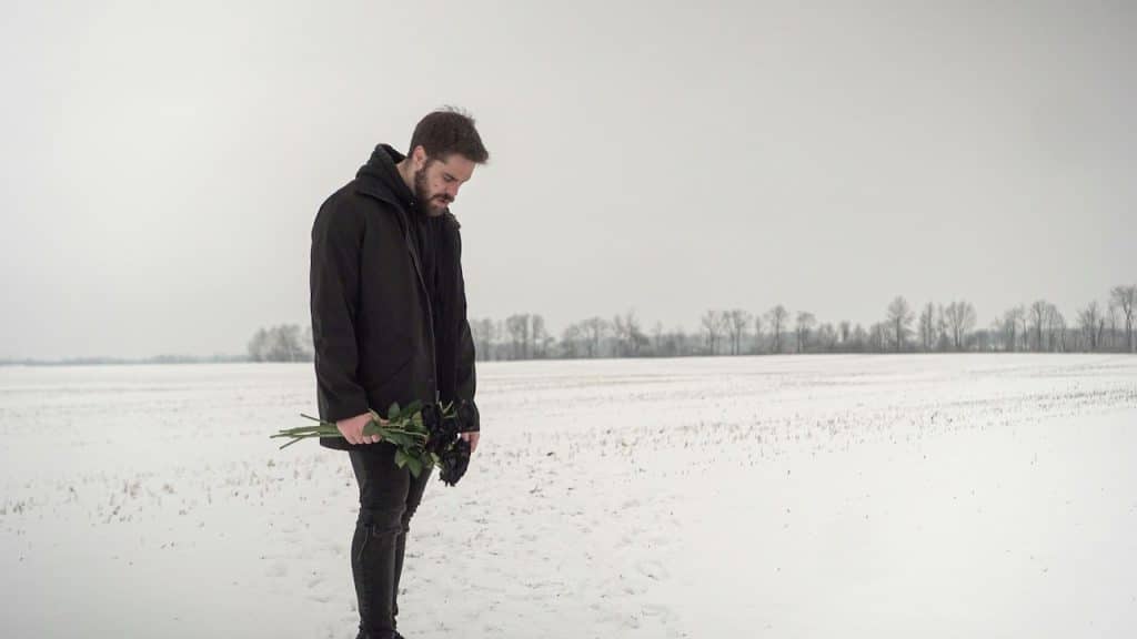 A man standing in the snow holding a bouquet of flowers.