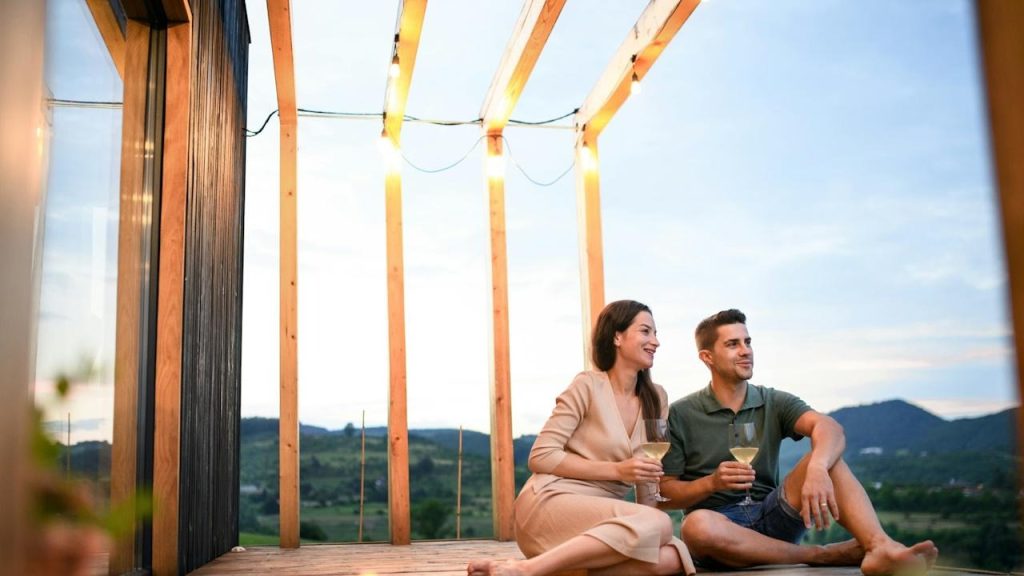 A young couple with wine sitting outdoors in a container house in the countryside.