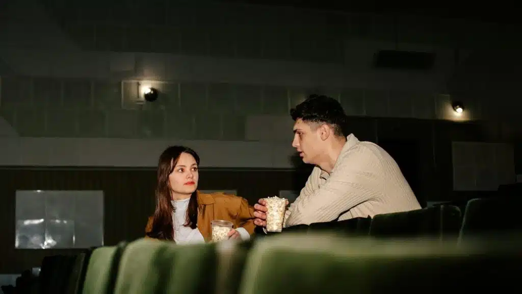 A couple eating popcorn while sitting in a cinema.