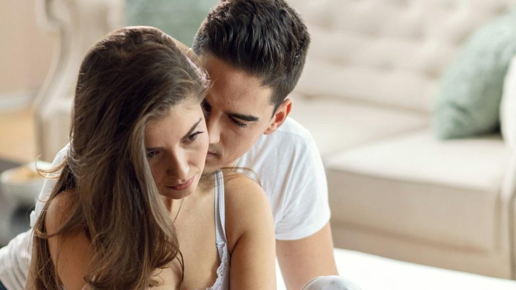 A young woman is feeling sad while her boyfriend is embracing her.