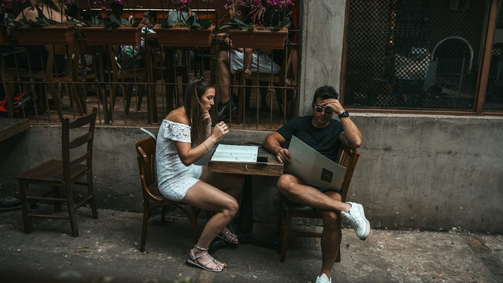 A man is reading a menu card while his wife is sitting silently at the table.