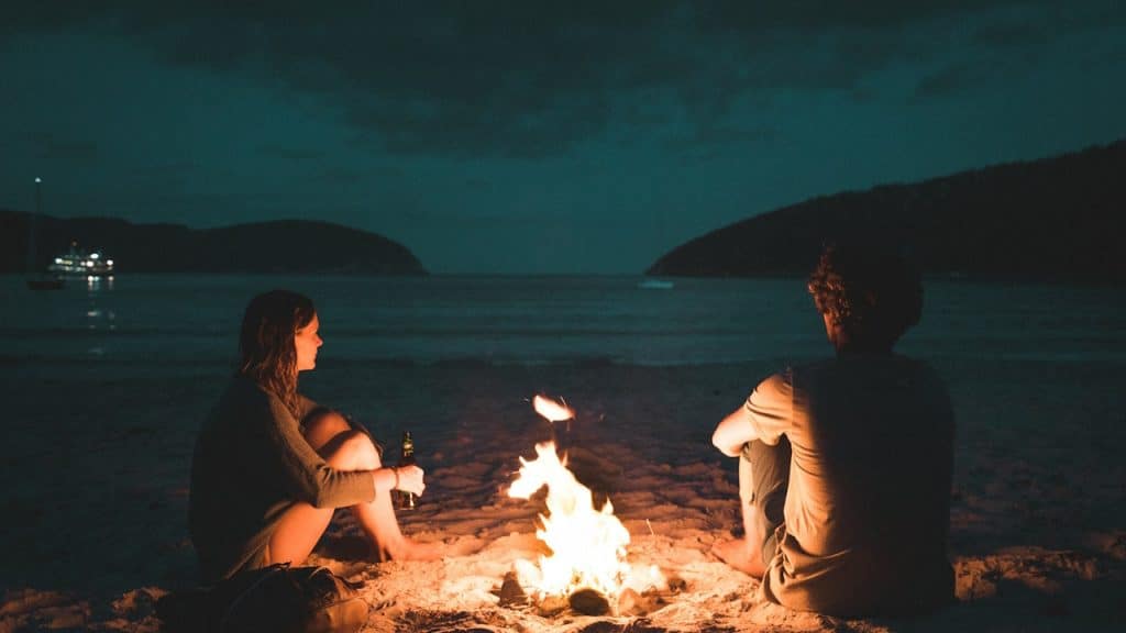 A couple sitting by a fire on a beach.