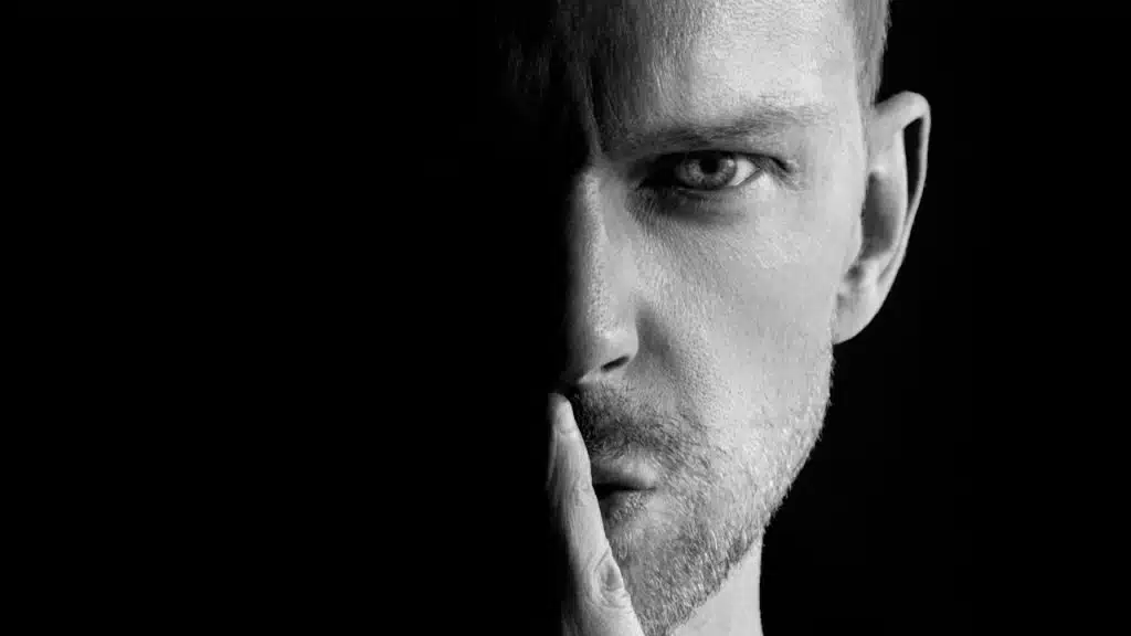 A man holding a finger to his lips telling someone to be quiet.
