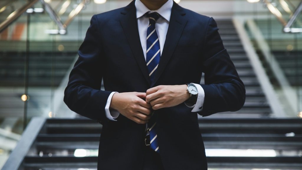 A person in a suit standing near the stairs.