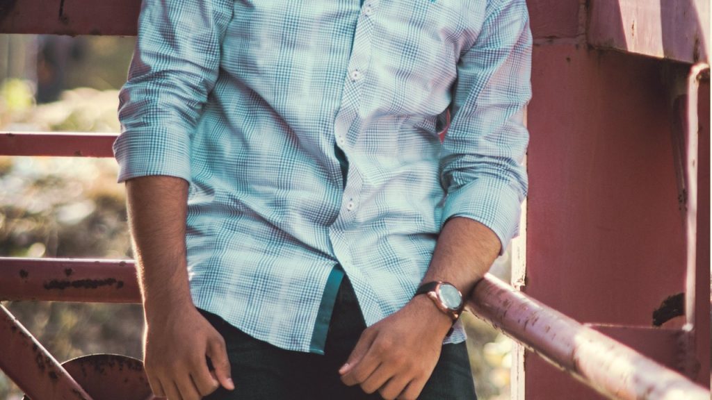 A man in a blue dress shirt standing beside a brown steel fence.