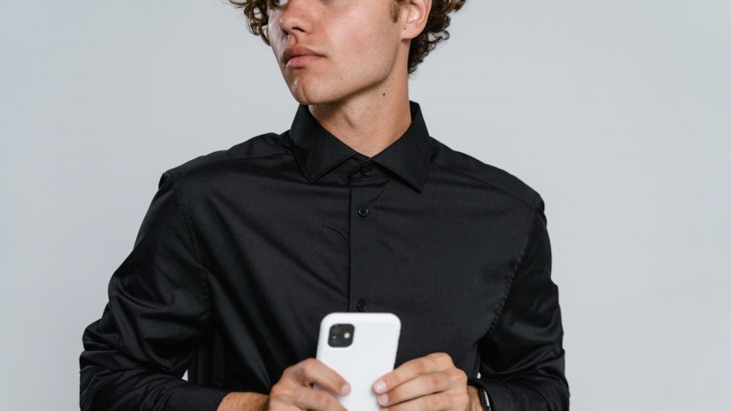 A man in a black dress shirt holding a white iPhone.