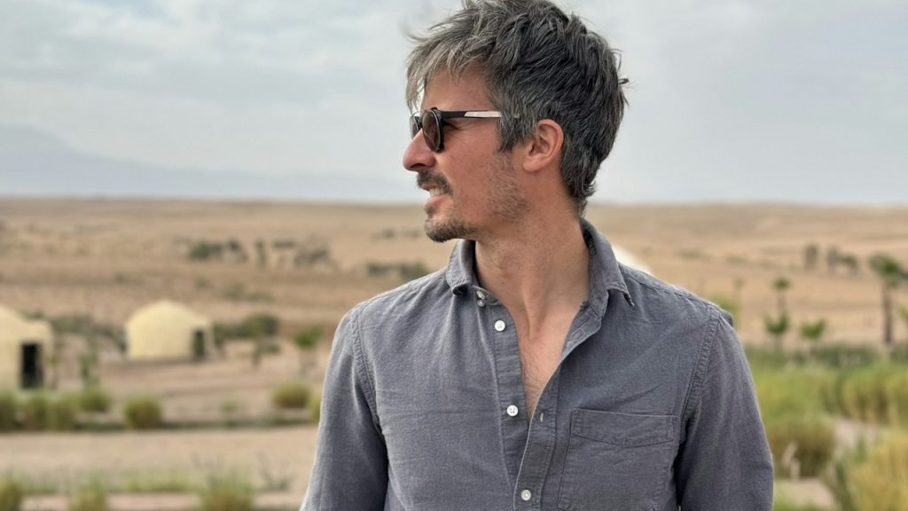 A man in sunglasses and a button-up shirt in a desert landscape.