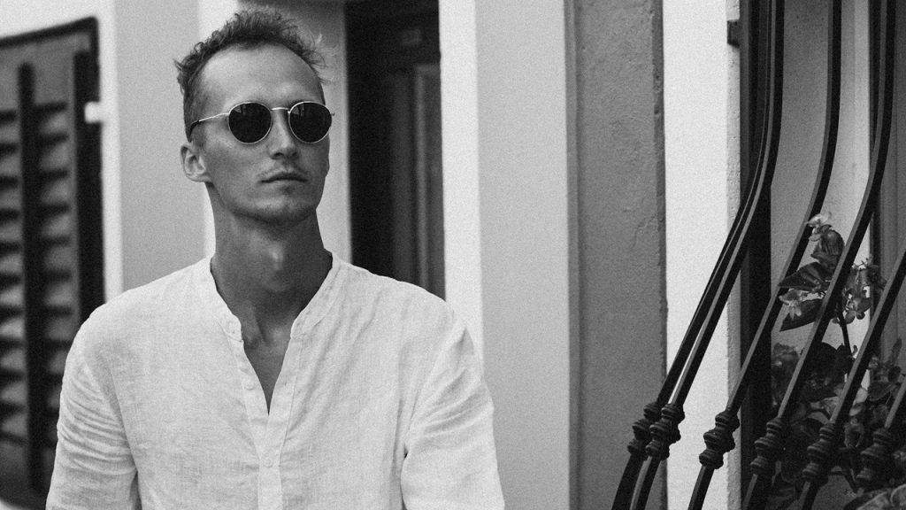 A man in a white shirt and sunglasses walking down a hallway.