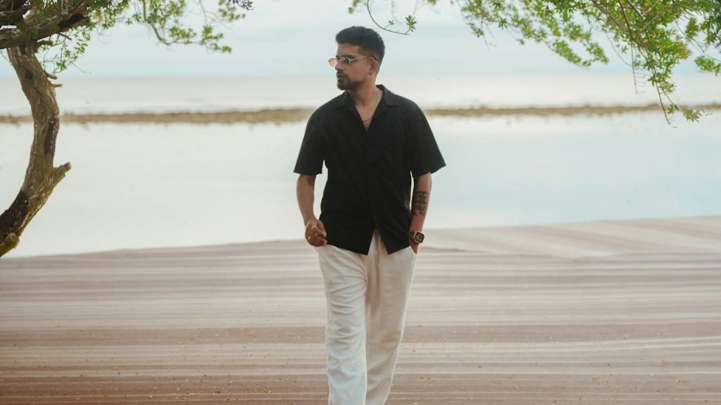 A man in a black shirt walks on a wooden path near water.