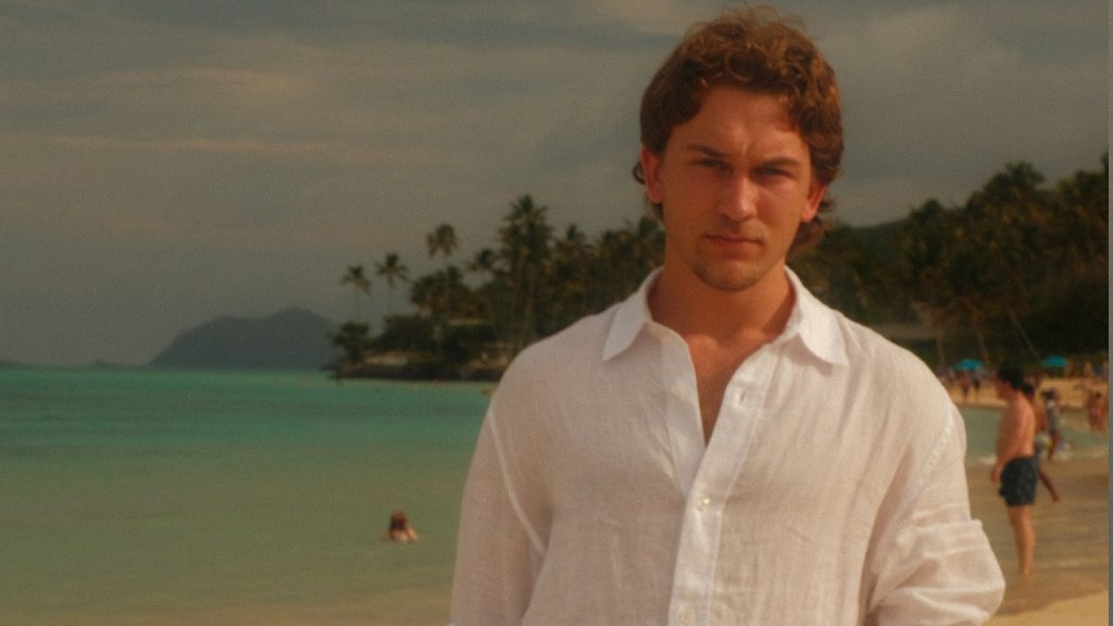 A man in a white shirt on a tropical beach.