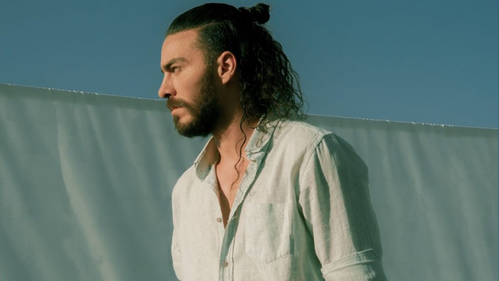A trendy-brutal man with a modern hairstyle squinting.