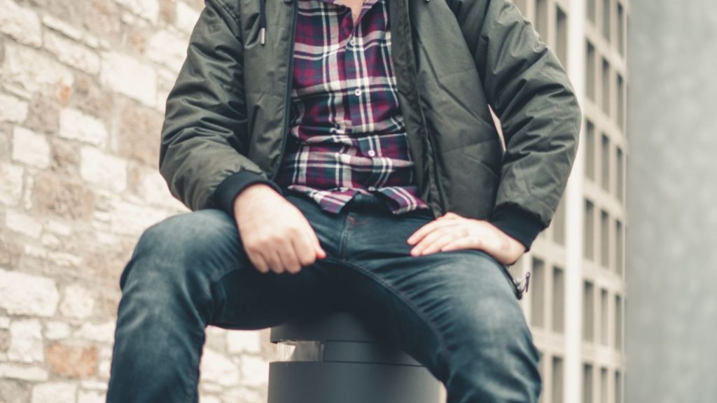 A man in a green jacket sitting on a bollard.