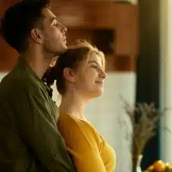 A man holding a woman close while she smiles and looks out of a window.