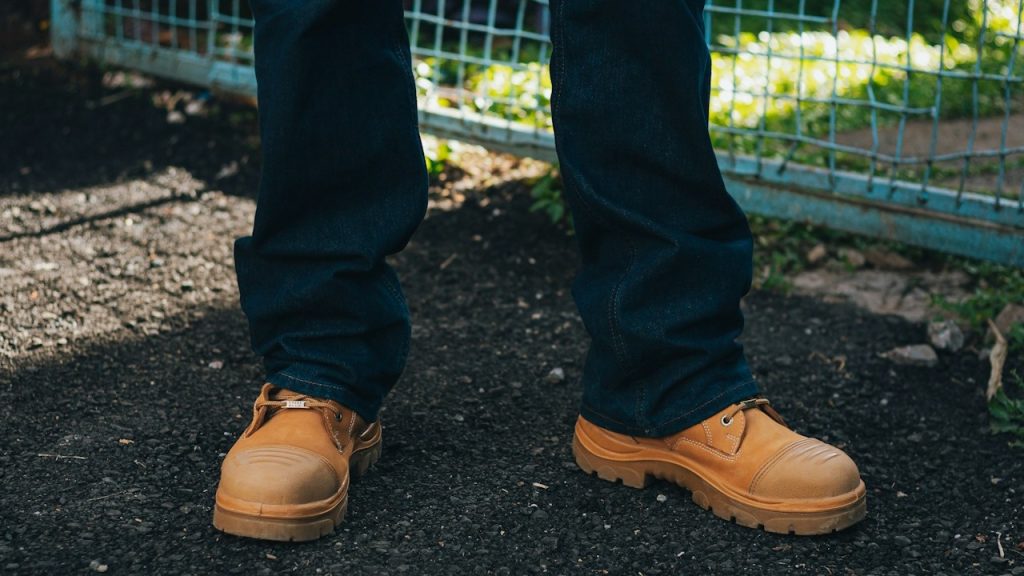 A person wearing dark denim jeans and tan work boots.