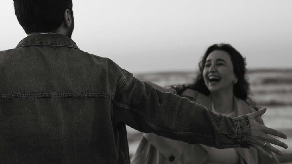 A man with open hands standing in front of a laughing woman who is coming towards him.