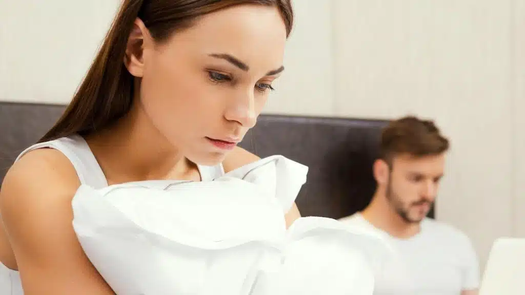 A woman looking sad while a man works on his laptop in the background.