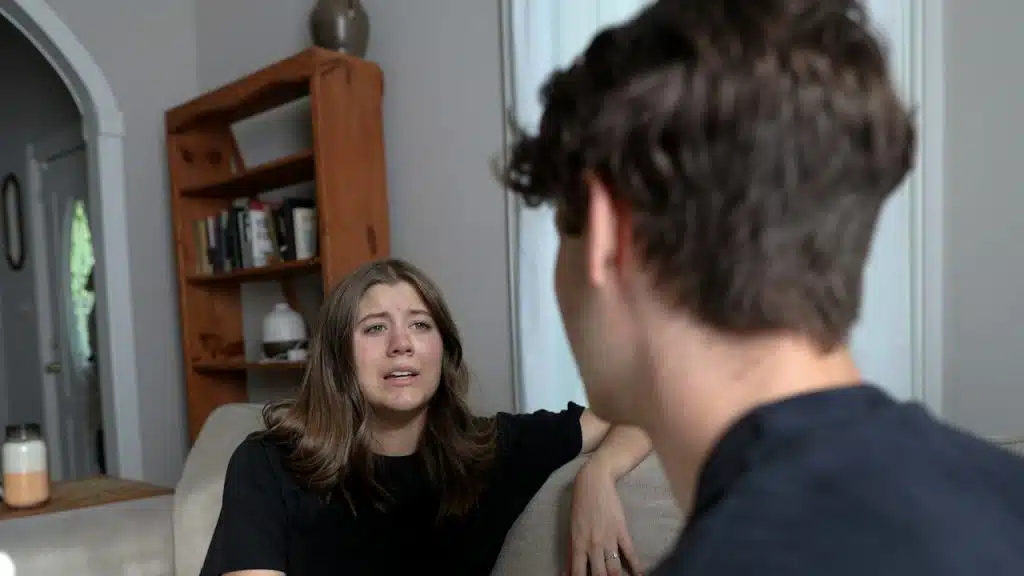 An upset woman looking at a man while they sit on a couch.