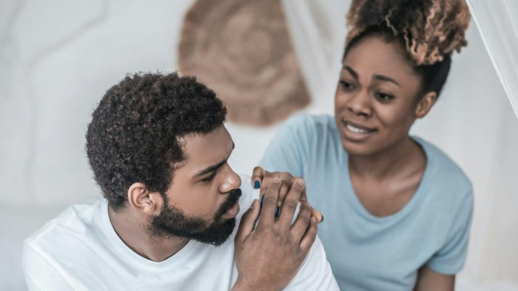 A woman apologizing to a man who is holding her hand to reassure her.