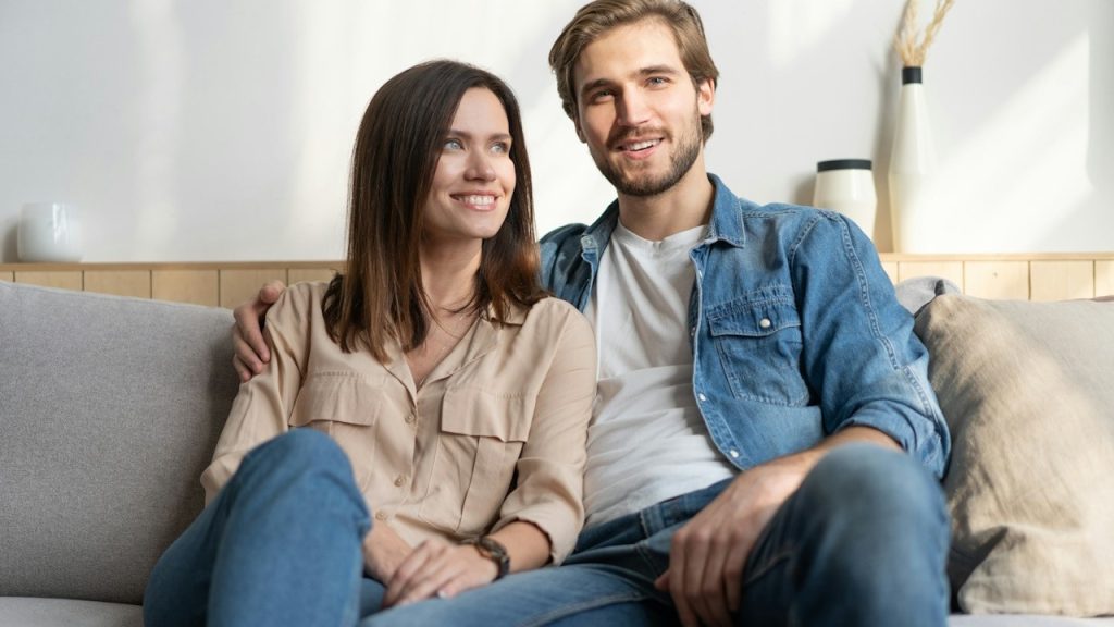 A smiling couple sitting on a couch together.