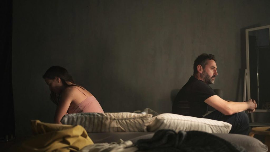 A man and a woman sitting separately on a bed.