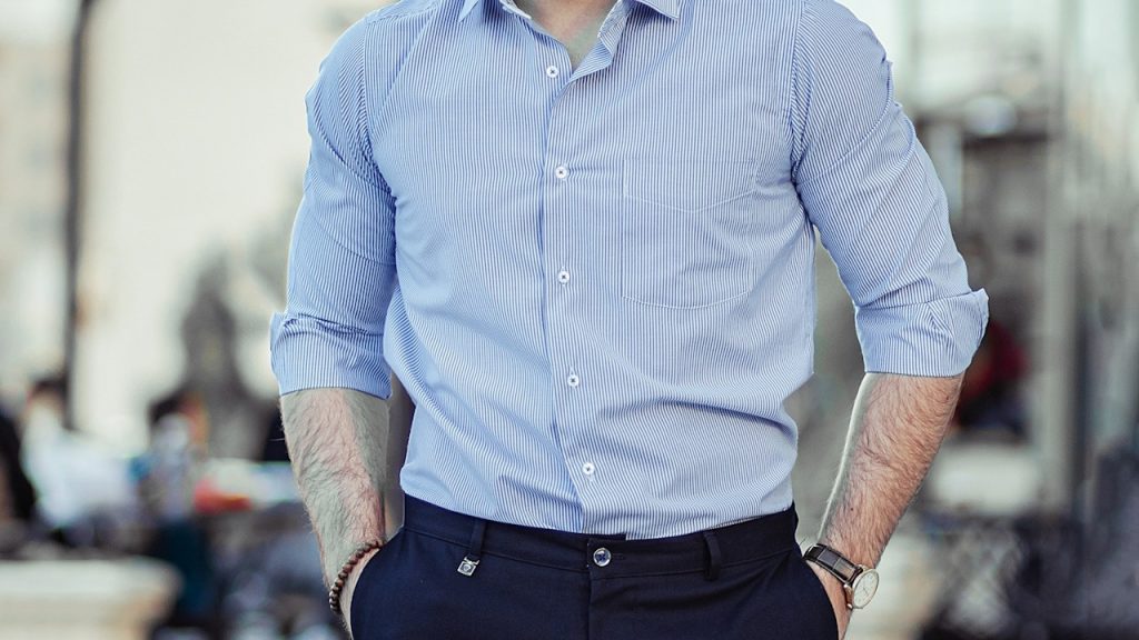 A man in a blue dress shirt and black dress pants standing.