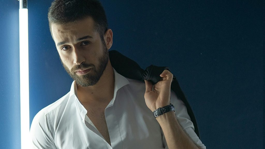 Man in a white dress shirt and blue denim jeans holding a black jacket
