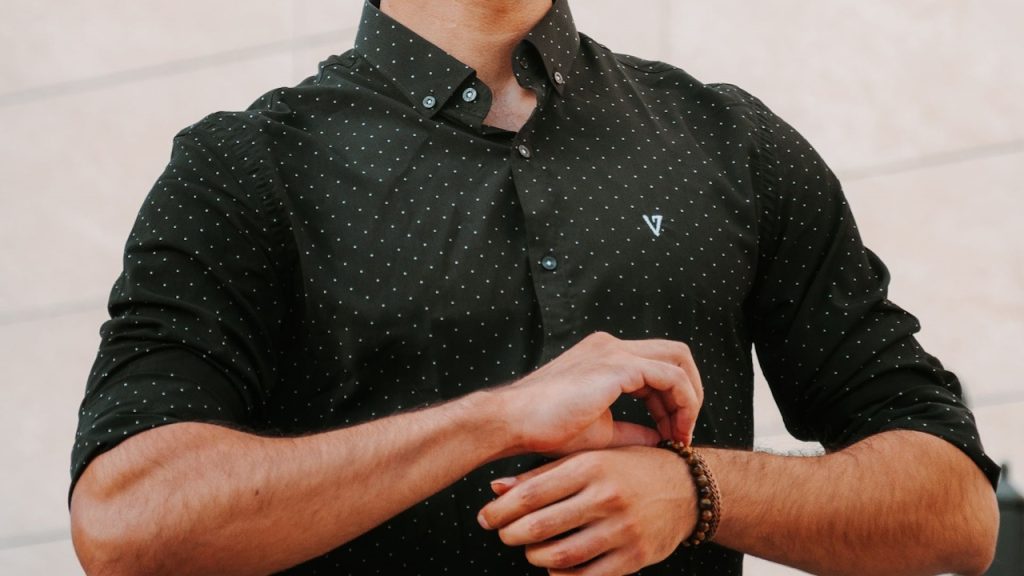 A man in a black shirt and jeans is touching his bracelets.