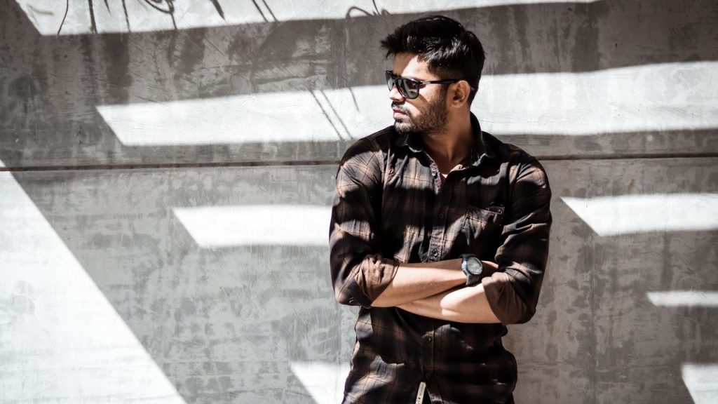 A man in casual wear posing by the gray wall.