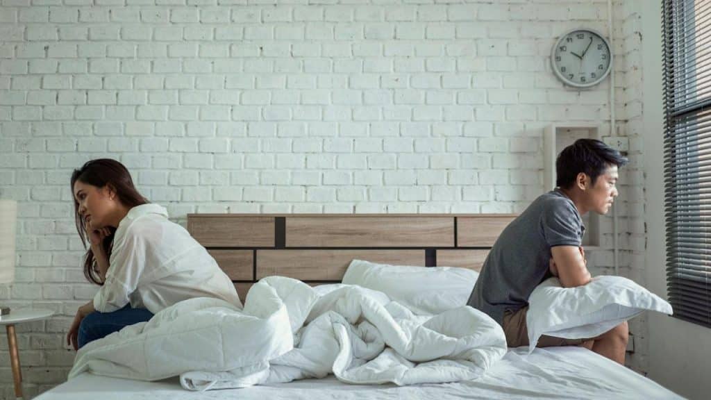 A couple sitting apart from each other on a bed with their backs to each other.